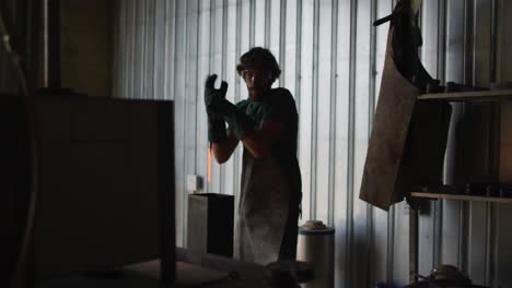 caucasian male blacksmith holding hot metal tool in kiln with tongs in workshop