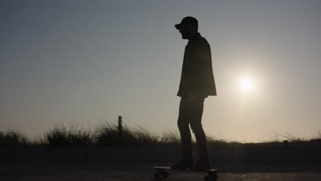 Cooler-Skateboarder-Fährt-Die-Straße-Entlang,-Die-Hinterleuchtete-Sonne-Kreiert-Eine-Silhouette