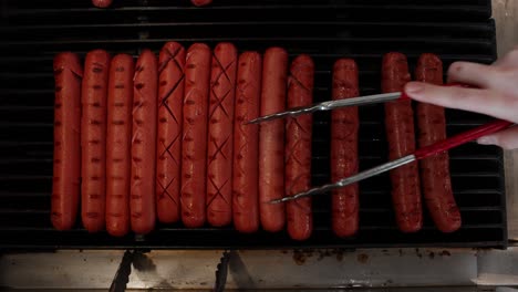 mano con pinzas cocinando y rodando perritos calientes en la parrilla