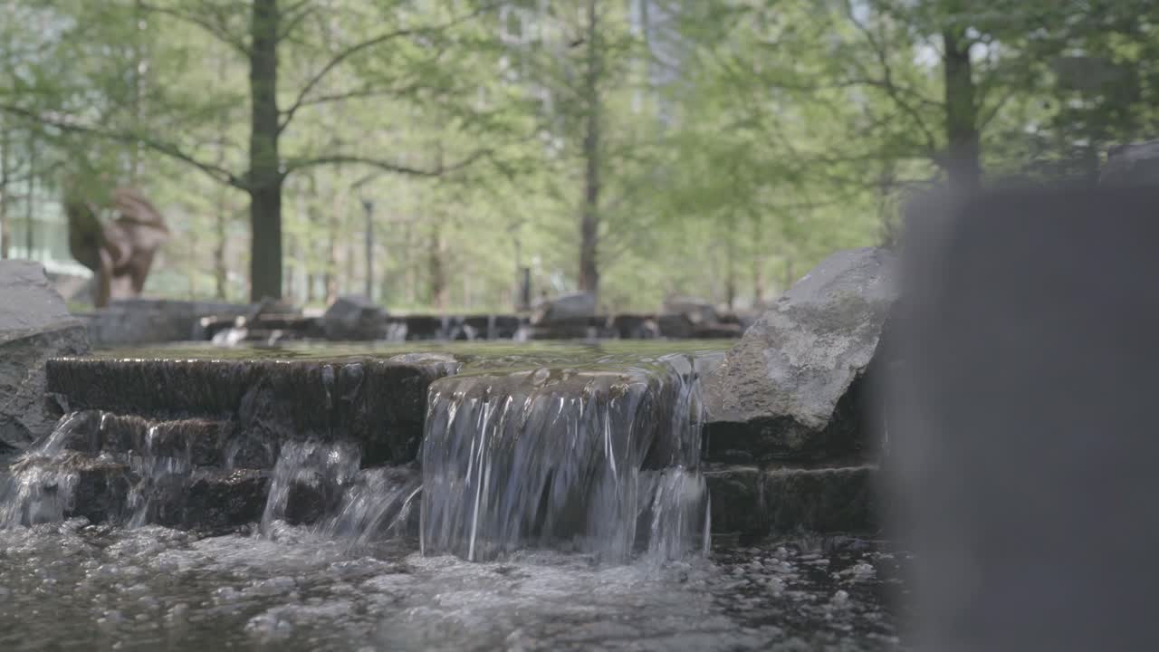 Small pond in Canary Wharf London with a stream of water over the mossy rocks is pleasing and relaxing under the green trees