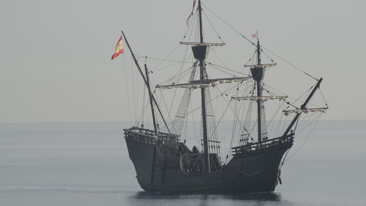 ferdinand magellan nao victoria carrack 보트 복제품과 스페인 국기가 있는 보트 복제품은 슬로우 모션 60fps로 잔잔한 바다 쪽에서 일출 시 지중해에서 항해합니다.