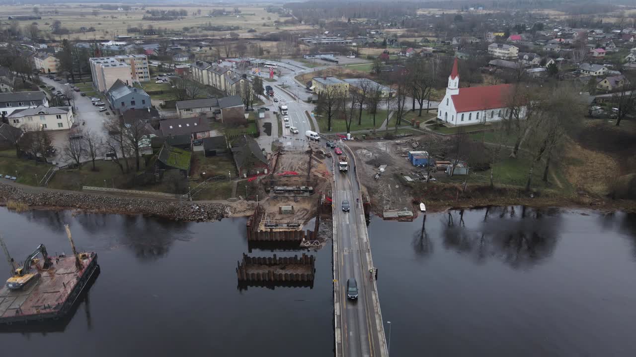 Aerial view of Salacgriva city in Latvia, featuring a river, a partially constructed bridge, and surrounding urban landscape. Ideal for infrastructure and urban studies.