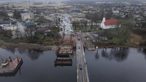 vista aérea de la ciudad de salacgriva en letonia, con un río, un puente parcialmente construido y el paisaje urbano circundante. ideal para infraestructura y estudios urbanos.