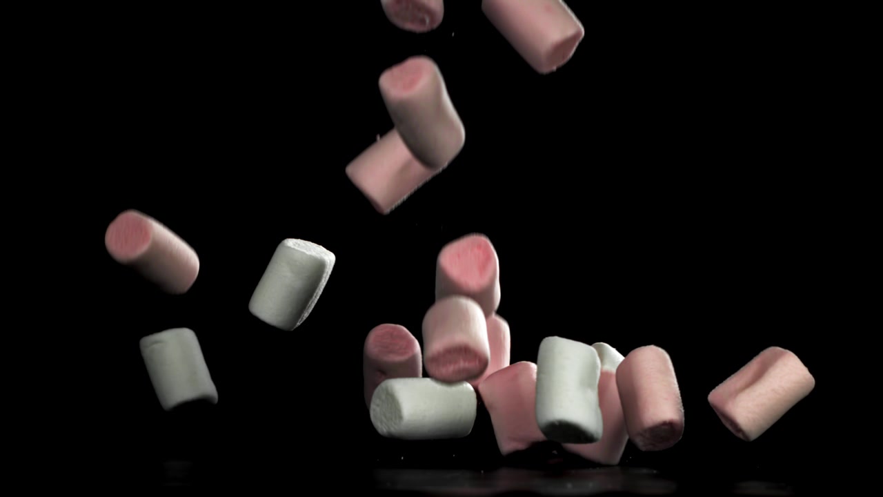 Marshmallow rosa e bianchi che cadono al rallentatore su sfondo nero.