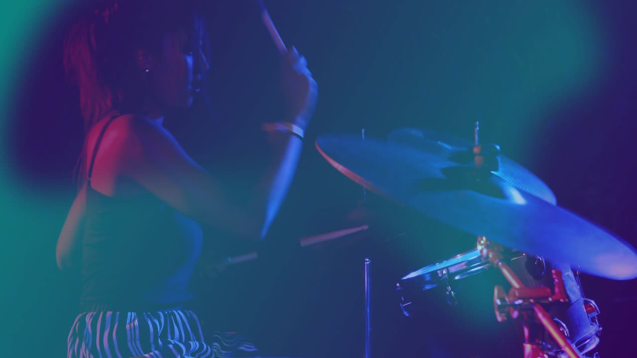 Batterista femmina che alza le bacchette, eseguendo rapidi colpi sul piatto ride tra una foschia verde acqua e magenta per la musica.