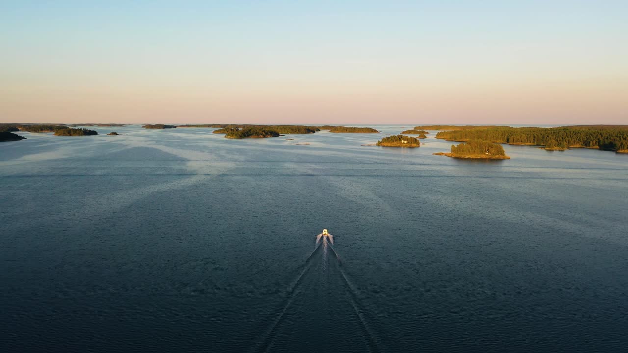 Aerial view of a boat, driving in middle of islands, colorful, summer sunset, in the Swedish archipelago, at the Gulf of Bothnia, in Sweden - Dolly, drone shot