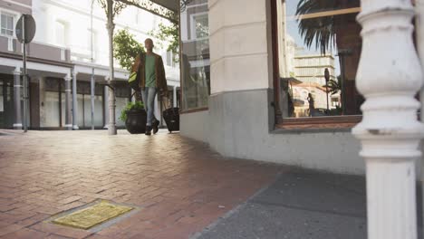 Mixed-race-man-walking-with-backpack-and-suitcase-in-the-street