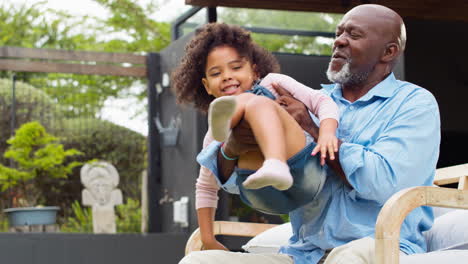 Abuelo-Divirtiéndose-Jugando-Con-Su-Nieta-En-El-Jardín-Levantándola-En-El-Aire