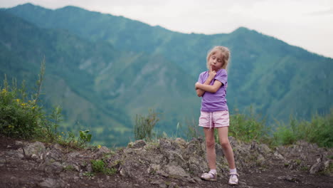 funny little child touches cheek with finger on rocky hill