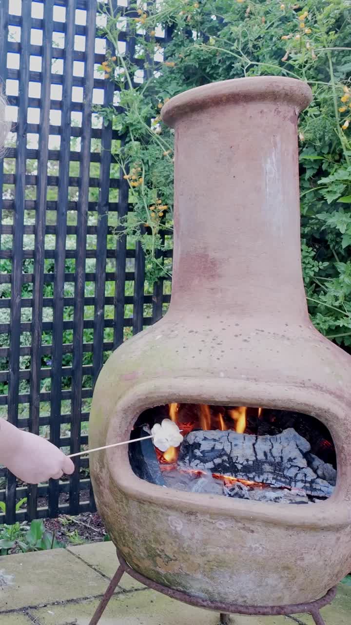 Toasting marshmallows over chiminea barbecue fire by hand VERTICAL shot
