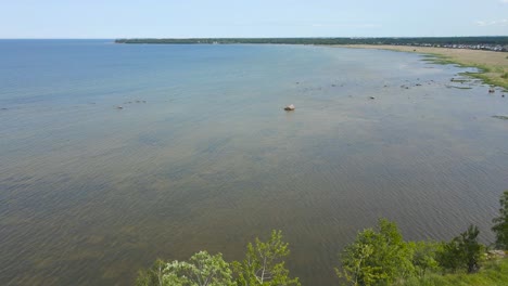 gorgeous aerial drone footage ascending and flying higher in front of a steep cliff bank that has a large blue ocean behind it during a summer sunny day. green bushes and trees grow on the limestone.