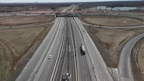 Das-Automatisierte-Stadtbahnsystem-Réseau-Express-Métropolitain-REM-In-Brossard,-In-Der-Nähe-Der-Stadt-Montreal,-Fährt-Auf-Der-Hauptautobahn-Mit-Auto--Und-LKW-Verkehr,-Luftaufnahmen-Von-Drohnen