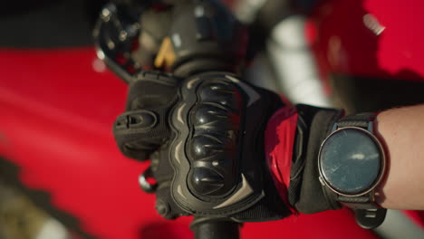 close-up of a biker s hand wearing protective gloves while using two fingers to hold and release the clutch lever on a motorcycle, a smartwatch is visible on the wrist