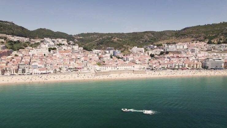Persone che si godono la spiaggia di sabbia, le pittoresche case di Sesimbra sullo sfondo di colline e cielo blu