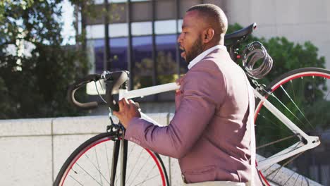 African-american-man-in-city-holding-bike-and-walking