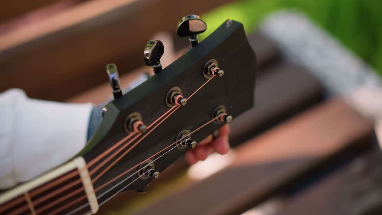 white hand tuning acoustic guitar outdoors wearing fingerless brace, closeup headstock with bronze strings, warm bokeh background, bench setting, gentle sunlight, musician practicing recovery