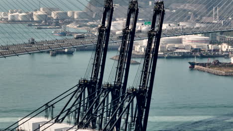 slow motion tracking left wide aerial drone shot of deep sea loading cranes with suspension bridge in the background during the day