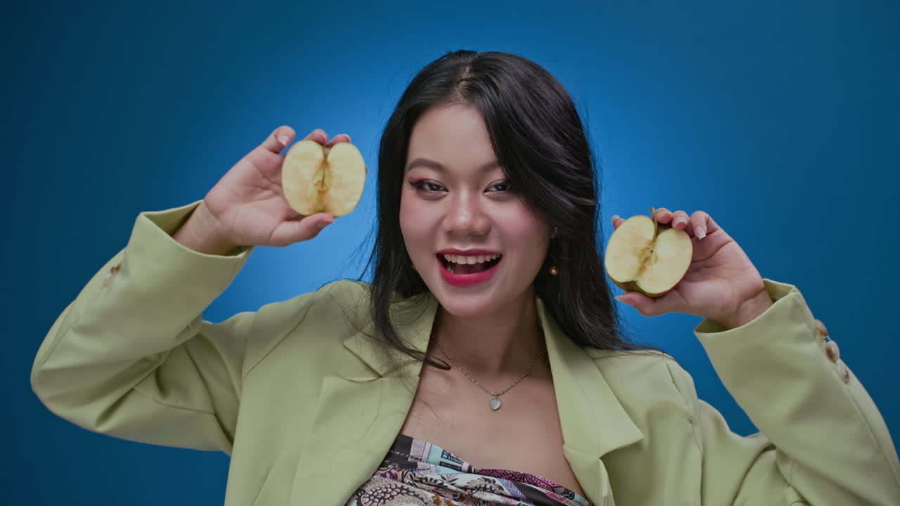 Portrait of Asian Girl Showing Apple Halves to Camera Isolated on Blue