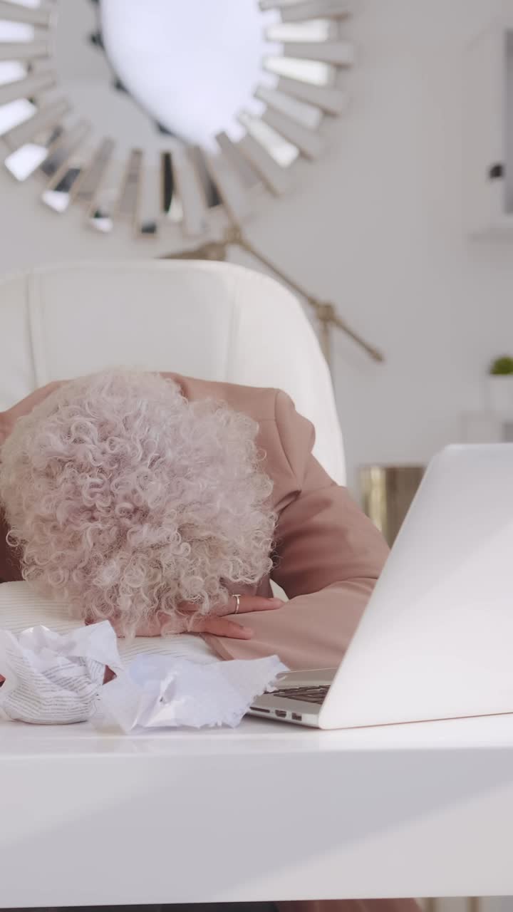 Stressed businesswoman with head on desk surrounded by crumpled paper