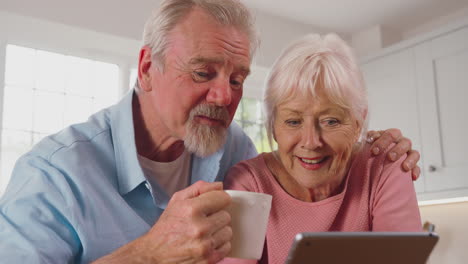 close up de una pareja de ancianos jubilados sentados en la cocina en casa bebiendo café y usando una tableta digital