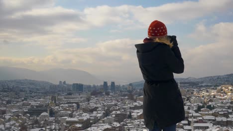 medium shot of a blonde woman's back view while looking over the city of sarajevo