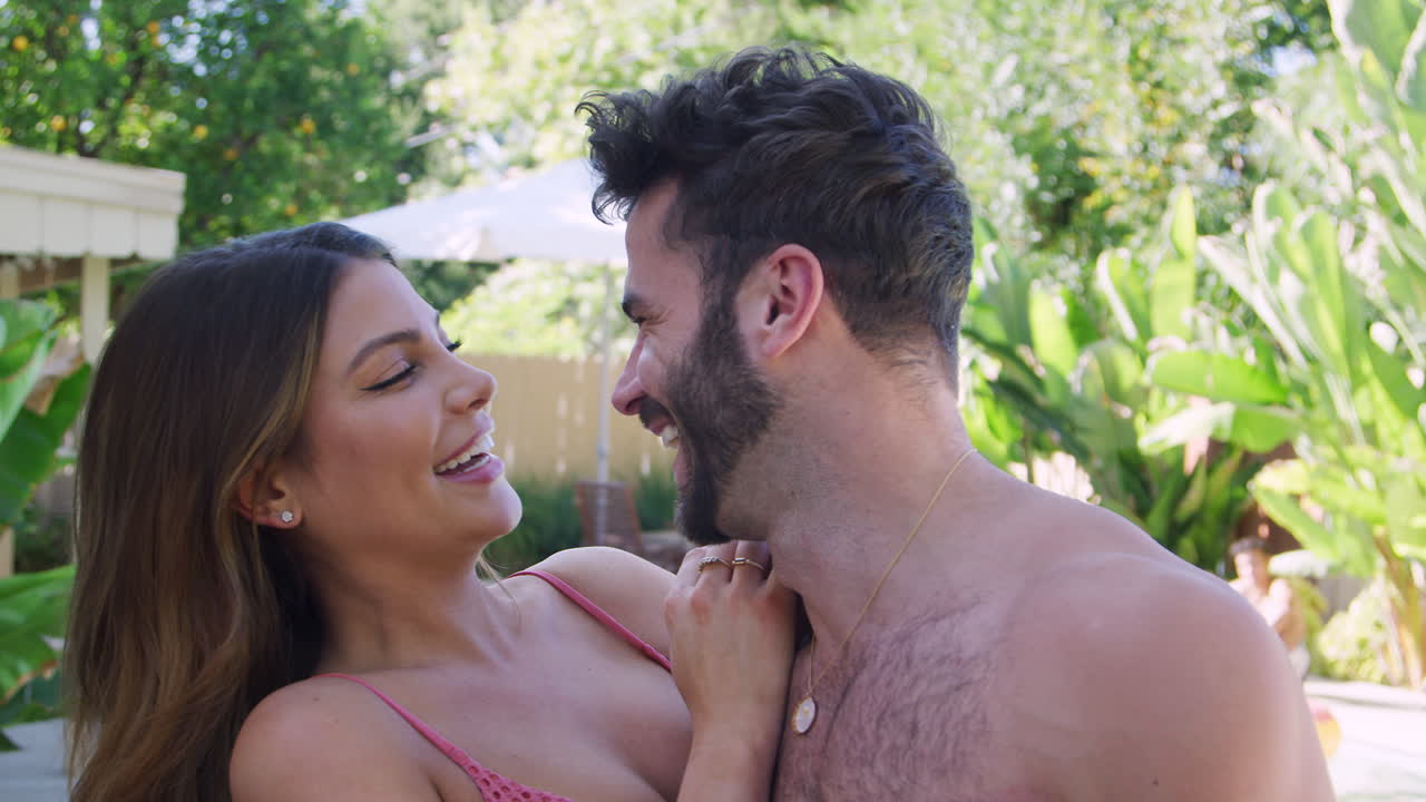 Portrait Of Romantic Hispanic Couple Outdoors With Friends Enjoying Summer Pool Party