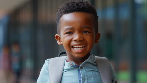 retrato de un alumno de escuela primaria sonriente al aire libre con una mochila en la escuela