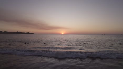 aerial drone over people at beach with sunset over ocean horizon, 4k