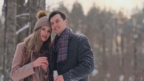 couple in love in the winter forest to drink tea from a thermos. stylish man and woman in a coat in the park in winter for a walk.