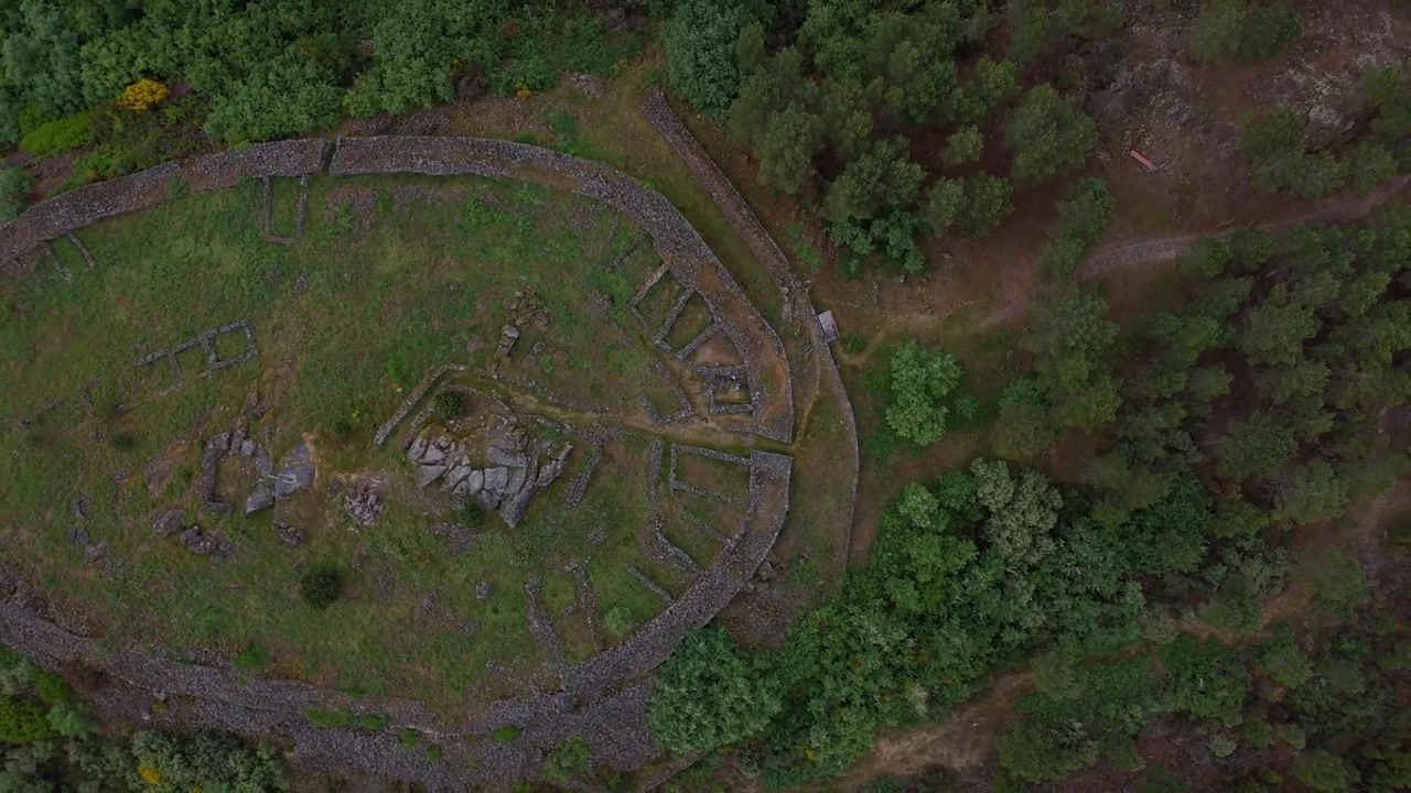 Ripresa orizzontale con drone che si eleva in orbita sopra il Castro de Curalha a Chaves, Portogallo, rivelando antiche rovine, la foresta circostante e il paesaggio