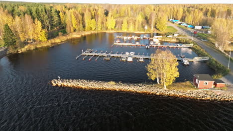 sweden - boats in a lakeside harbor with a forest backdrop on a breezy october day, as the setting sun bathes the scene in warm, vibrant autumn colors - aerial drone