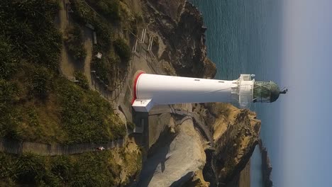 a reversing vertical drone shot of a person jogging along a wooden pathway away from a beautiful white lighthouse