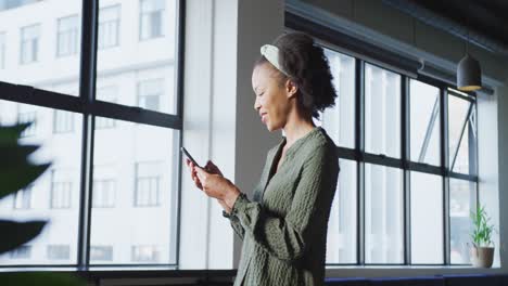 Afroamerikanische-Geschäftsfrau-Am-Fenster,-Die-Allein-Im-Büro-Ihr-Smartphone-Benutzt