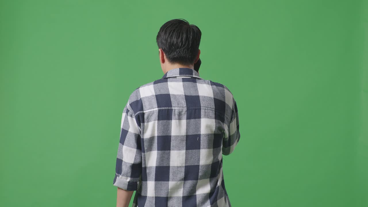 스튜디오에서 녹색 화면에서 는 동안 휴대 전화로 이야기하는 아시아 남자의 뒷면
