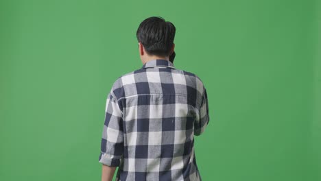 스튜디오에서 녹색 화면에서 는 동안 휴대 전화로 이야기하는 아시아 남자의 뒷면
