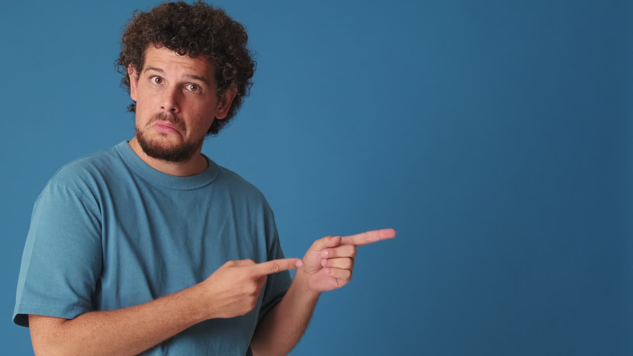 Man with Curly Hair Pointing to Copy Space on Blue Background