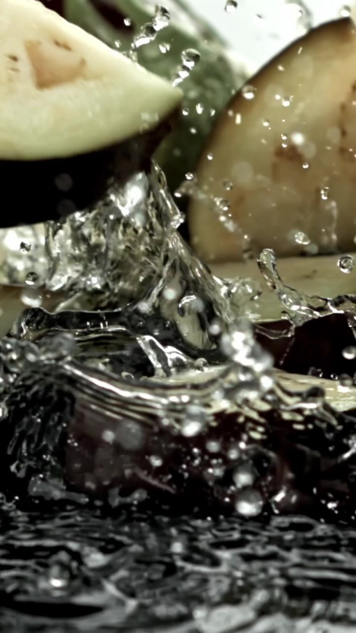 Fette di melanzana fresca che schizzano nell'acqua al rallentatore