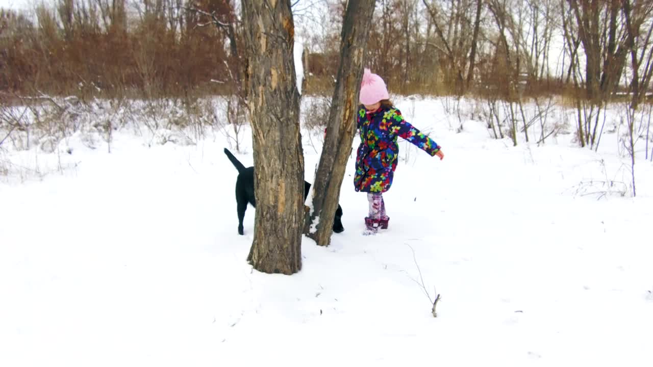 niña jugando con su labrador negro en la nieve