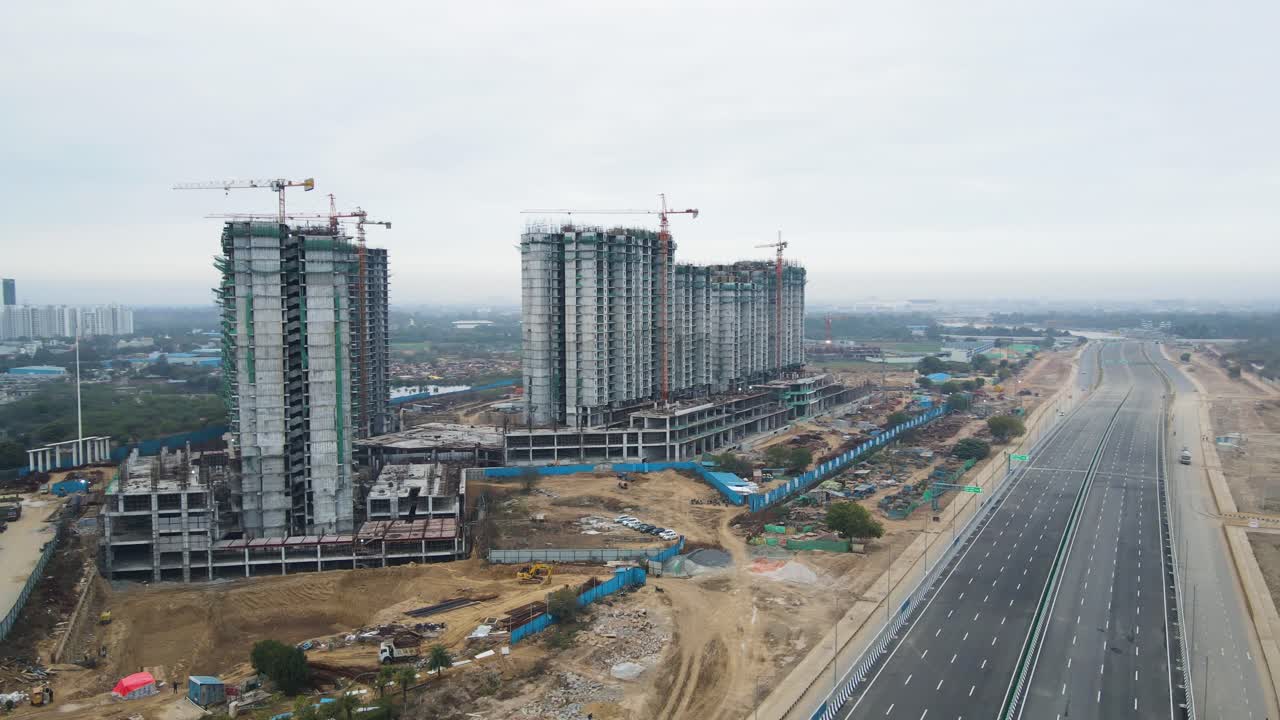 Aerial drone shot revealing the skeletal framework of a high-rise under construction near Dwarka Expressway, with concrete pillars and exposed steel reinforcements.