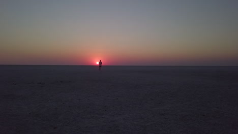 low dolly aerial of man watching golden sunset on flat salt pan