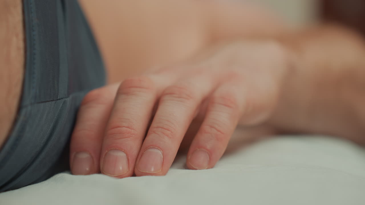 closeup hand resting on massage bed, male client awaiting microcurrent treatment, fingers relaxed on white linen, soft ambient lighting, clinical calm, shallow depth of field focusing on fingertips