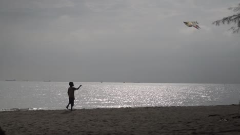 Silueta-De-Niño-Jugando-Y-Volando-Cometas-En-La-Playa-Con-Reflejo-De-La-Luz-Del-Sol-En-El-Fondo-Del-Mar