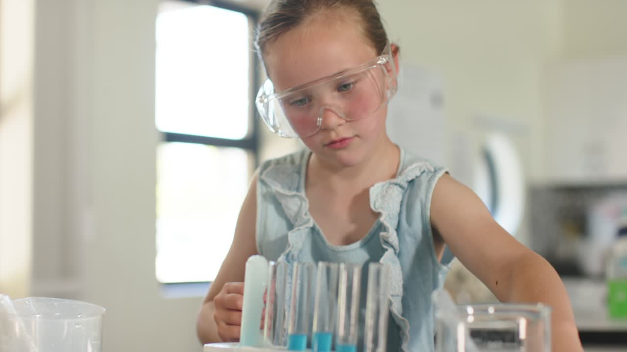 Pige med beskyttelsesbriller lægger mærke til et bæger og bruger en pipette til at tilsætte væske i reagensglas på køkkenbordet derhjemme til et videnskabeligt eksperiment