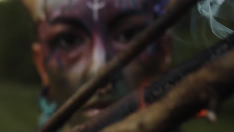 Closeup-of-a-fire-Mystical-performer-in-tribal-face-paint,-holding-a-flaming-burning-stick