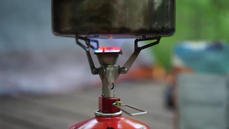 estufa de camping ardiendo agua hirviendo con el hombre colocando el paquete de alimentos en segundo plano.