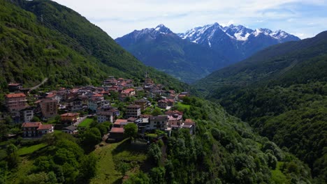 aerial view of malonno village perched on green hillside above valley forest, with alps in distance. shot at malonno, italy (italia)
