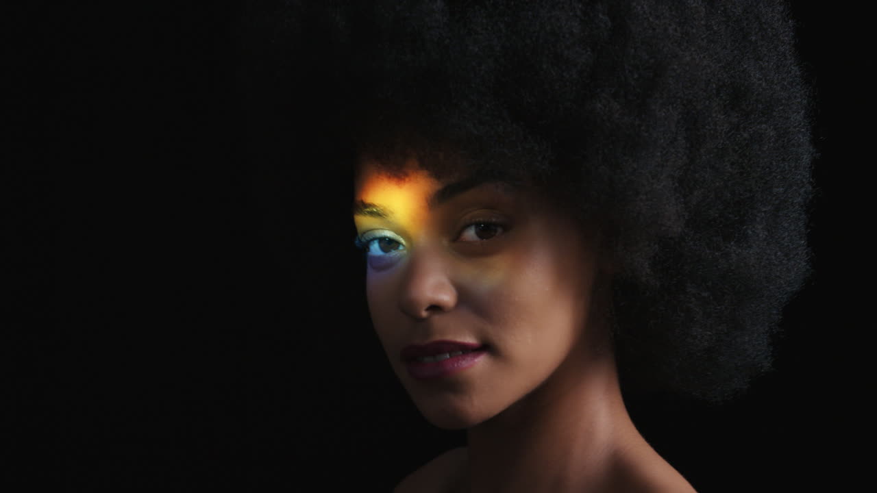 ritratto multicolore ravvicinato bella donna afroamericana con afro che gode di una pelle liscia e sana che sembra sicura bellezza naturale luce colorata su sfondo nero concetto di cura della pelle