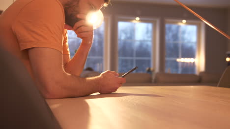 Man-sits-at-table-at-home-looking-at-mobile-phone-with-anxious-expression