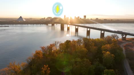 Sunrise-over-Memphis,-with-electric-car-charging-icon-on-bridge-over-the-Mississippi-River