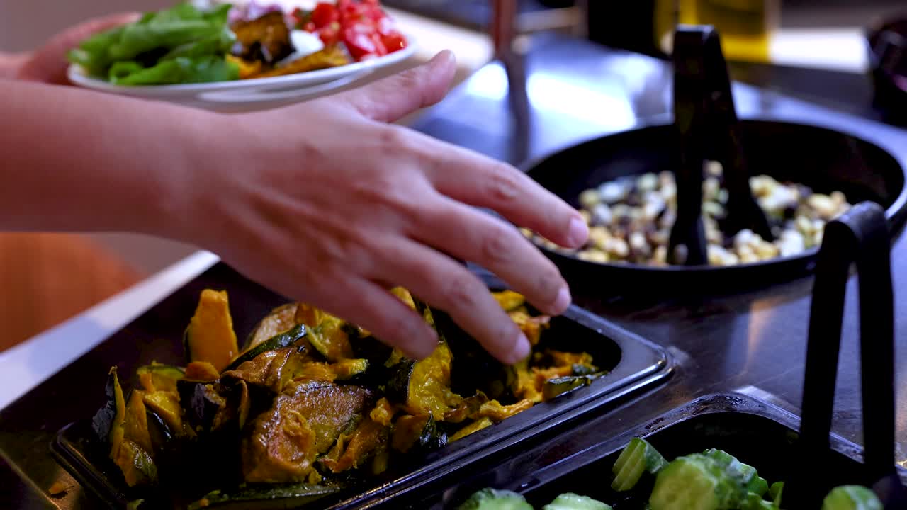 Customer uses tongs to add roasted pumpkin to salad plate at buffet-style bar